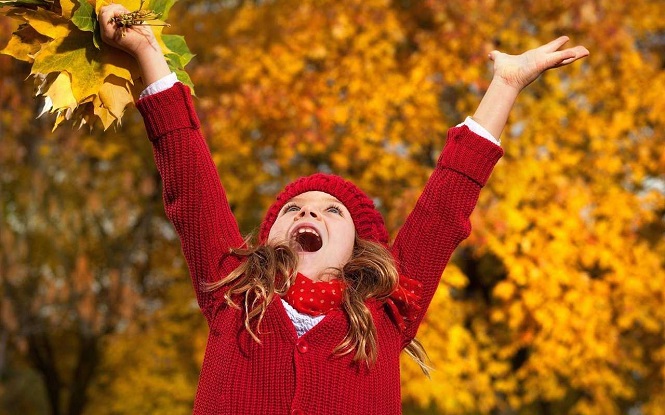 Девочка радуется опавшей листве в парке